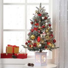 a small christmas tree with red, gold and silver ornaments in a living room window sill