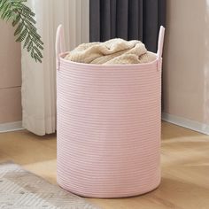 a pink laundry basket sitting on top of a wooden floor next to a potted plant