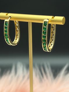 Emerald gold hoop earrings feature a circular design crafted in gold, adorned with multiple small, vivid green emeralds set along the outer edge. The emeralds sparkle elegantly, contrasting beautifully with the warm hue of the gold, creating a luxurious and sophisticated piece of jewelry. Party Green Gold-plated Earrings, Green Gold Plated Round Earrings, Green Round Gold-plated Earrings, Green Gold-plated Round Earrings, Elegant Round Hoop Earrings With Emerald, Green Formal Hoop Earrings, Formal Green Hoop Earrings, Green Gold-plated Pierced Earrings, Pierced Green Gold-plated Earrings