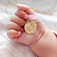 a baby's hand holding a tiny gold necklace