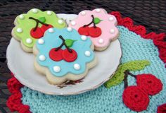 three decorated cookies sitting on top of a white plate next to cherries and berries