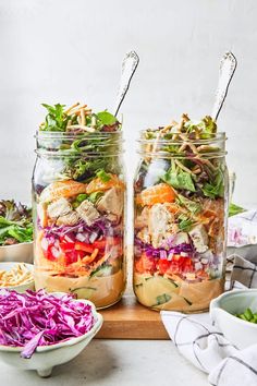 two mason jars filled with salads on top of a cutting board