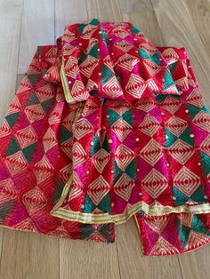 two pieces of red and green sari with gold trims on the bottom, sitting on