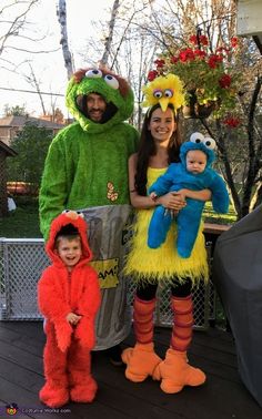 three people in costumes standing on a deck with one holding a small child and the other holding a stuffed animal