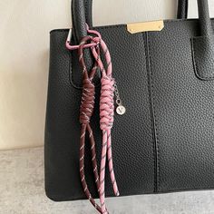 a black purse with pink and white braiding on the handle, hanging from a hook