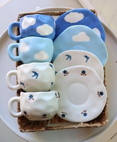 there are many cups and saucers in the basket on the table, including one with blue birds