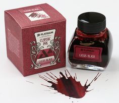 a bottle of ink sitting on top of a white table next to a red box