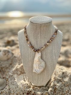 a necklace on a mannequin in the sand with shells and seashells around it