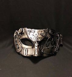 Upgrade your Steampunk costume with this awesome mask. This Steampunk mask is painted silver/black and accented with lots of gears and detail. Mask is light weight, durable, and comes with a 1" thick elastic band for a secure fit. Steampunk mask size 7"W x 3.5"H. Color antique silver and black. Black Steampunk Masks For Masquerade, Black Steampunk Masks And Prosthetics With Adjustable Fit, Black Steampunk Costume Mask, Black Steampunk Masks For Cosplay, Black Steampunk Mask Costume Accessory, Masquerade Ball Mask, Steampunk Mask, Ball Mask, Feather Mask