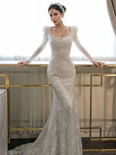 a woman in a long sleeved wedding dress standing next to a window with her hands on her hips