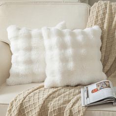 two white pillows sitting on top of a couch next to a blanket and a book