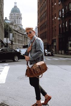 a man is walking down the street carrying a brown handbag in his right hand