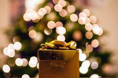 a christmas tree with lights in the background and a gold gift box sitting on a table