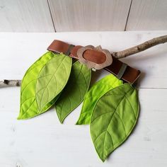 two green leaves on a branch with a brown leather belt hanging from it's end