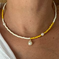 a woman wearing a yellow and white beaded necklace with pearls on the end of it