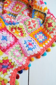 a crocheted blanket with multicolored squares and pom - poms