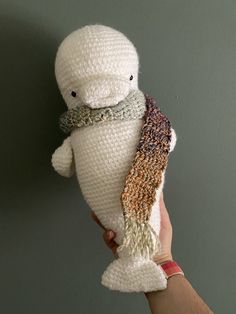 a hand holding a stuffed animal that looks like a fish with a scarf around its neck