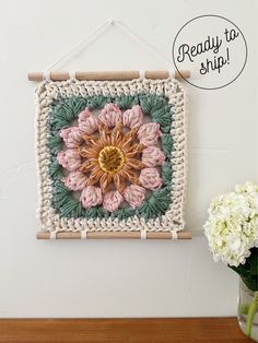 a crocheted wall hanging with a flower on it and a vase full of flowers