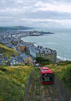 a red train traveling down tracks next to the ocean and buildings on both sides of it