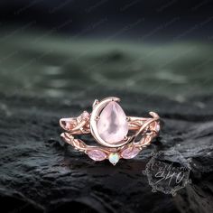 a rose quartz ring on top of a rock with water droplets and leaves around it