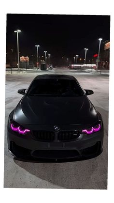 a black car parked in a parking lot at night with purple lights on the hood