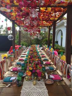 a long table with many plates and place settings on it, decorated with colorful flowers