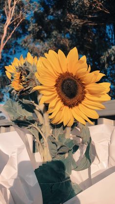 a large sunflower sitting in a vase on top of a white cloth covered table