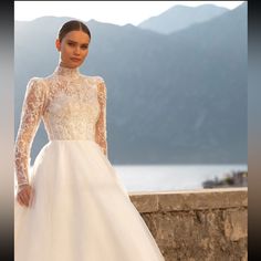 a woman in a white wedding dress standing on a stone wall with mountains in the background