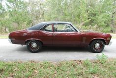 a red car parked on the side of a road in front of some grass and trees