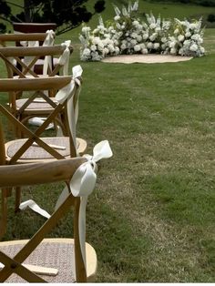 rows of wooden chairs sitting on top of a lush green field next to a white flower arrangement