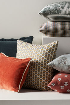 a bunch of pillows sitting on top of a white shelf in front of a wall