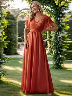 a woman wearing an orange dress standing in front of a green archway with greenery