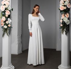 a woman in a long white dress standing next to some flowers and pillars with roses on them