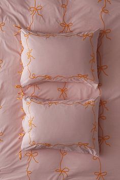 four pillows with orange bows on them sitting on top of a pink comforter covered bed