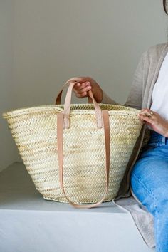 a woman sitting on a bench holding a large woven basket in her hands and looking at the camera