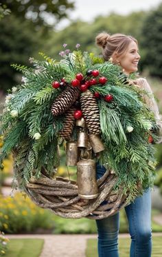 a woman carrying a christmas wreath with bells and pine cones on her back, in the middle of a garden