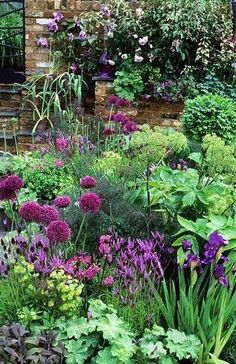 a garden filled with lots of different types of flowers and plants in front of a brick building