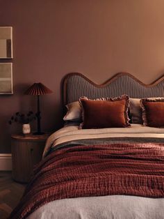 a bed with pillows and blankets on top of it next to a night stand in front of a wall