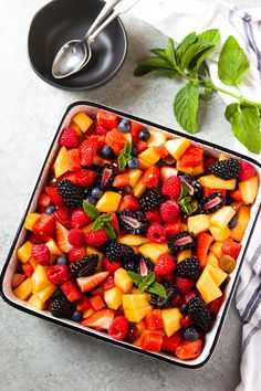 fresh fruit salad in a square dish with mint leaves and berries on the side, ready to be eaten