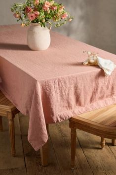 a pink table cloth with flowers in a white vase on the top and two wooden chairs