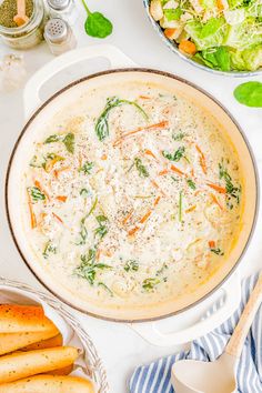 a bowl of soup with cheese, carrots and spinach in it next to some breadsticks