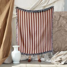 a large red and white striped blanket sitting on top of a table next to a vase