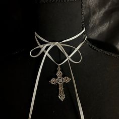 This necklace has a long white ribbon and a metal cross pendant, intended to be wrapped multiple times around the neck. It is about 62 inches long. Adjustable White Cross Necklace, Adjustable White Cross Necklaces, Adjustable Silver Cross Lariat Necklace, Elegant Cross Choker As A Gift, White Spiritual Crucifix Cross Necklace, White Crucifix Cross Necklace, Vintage White Cross Jewelry, Adjustable Silver Cross Choker, Elegant Silver Cross Choker