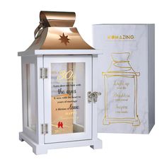 a white and gold lantern with a card in it next to a box for the candle