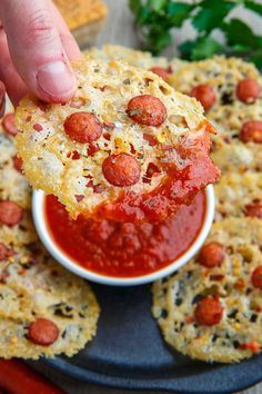 a person dipping some kind of pizza into a small white bowl filled with sauce on top of crackers