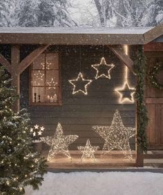 christmas lights on the outside of a cabin in the snow with stars hanging from the roof