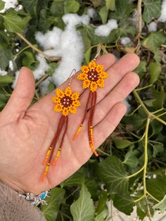 a hand holding two orange and yellow beaded flower earrings on it's palm