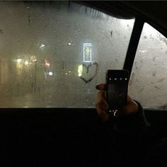 a person holding up a cell phone in front of a window with rain drops on it