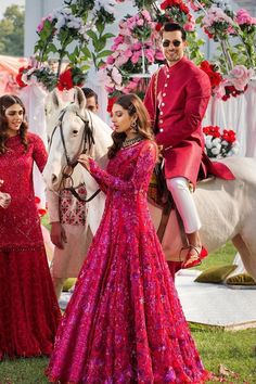 two women in red dresses standing next to a white horse and another woman in pink dress