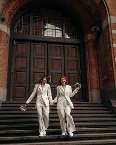 two women in white suits are walking down the stairs outside an old building holding hands